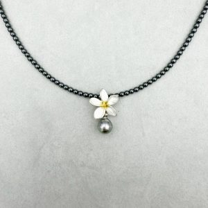 Schöne Kontraste: die silberweiße Frangipani Blüte mit Goldakzent und dazu eine kleine, tropfeiförmige Tahiti-Perle. Kombiniert ist der Anhänger mit einer Kette aus glänzendem Hämatit. Gesamtlänge: 45cm Tahiti-Perle: 10x8.5mm, gebändert, dunkles Silbergrau Farngipani-Blume: ca. 1.5cm Ø, 925/- Silber, teilweise vergoldet Kette: Hämatit Verschluss: Steckschließe 925/-Silber, eismatt