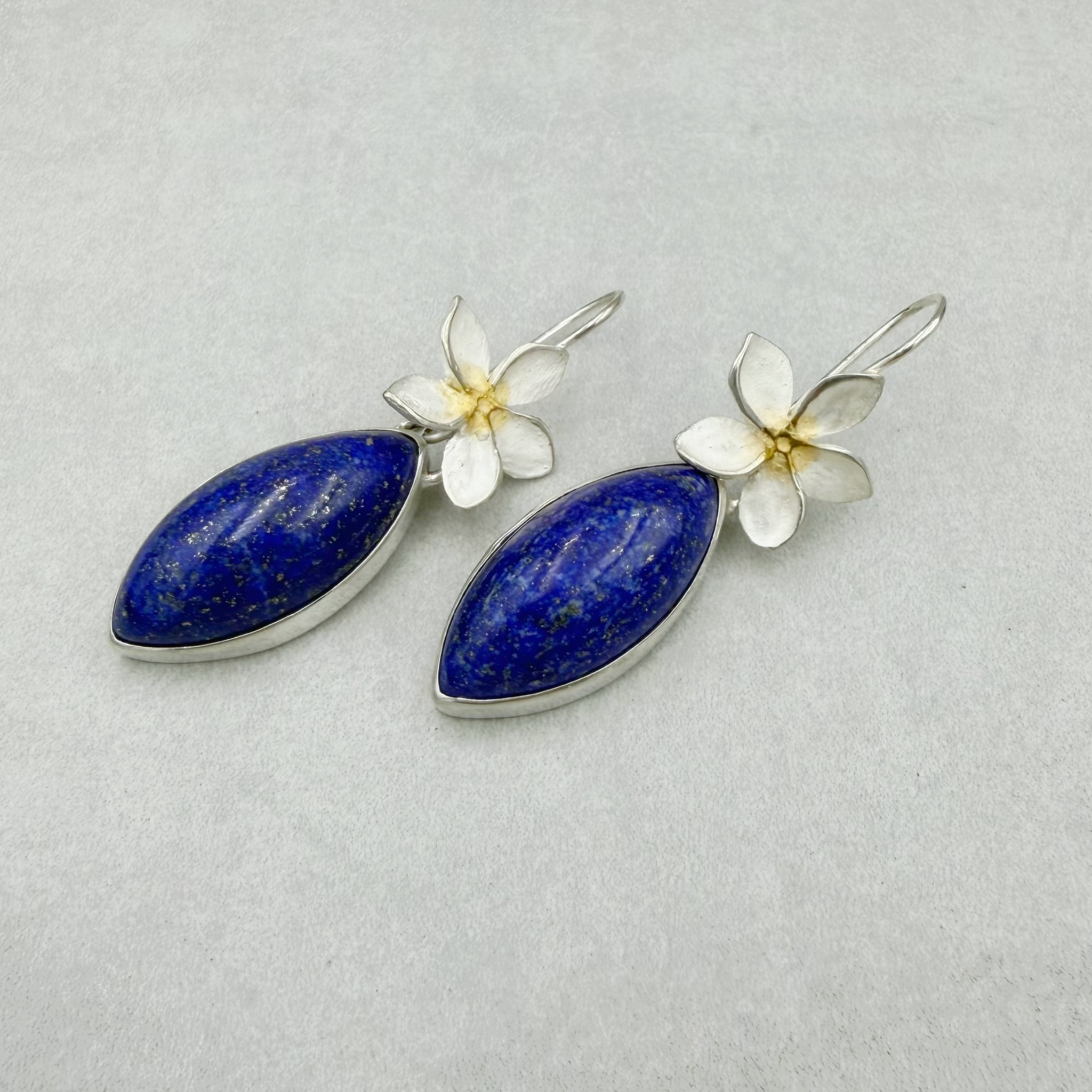 Ohrhänger mit Frangipani-Blüten und großen, blauen Lapislazuli-Navette-Cabochons. Die Edelsteine lassen sich von den Blüten trennen, so kann man die Blüten auch einzeln als kleine Ohrhänger tragen. Frangipani-Blumen: ca. 1.5cm, 925/-Silber, teilweise vergoldet Lapislazuli: je ca. 29x14mm