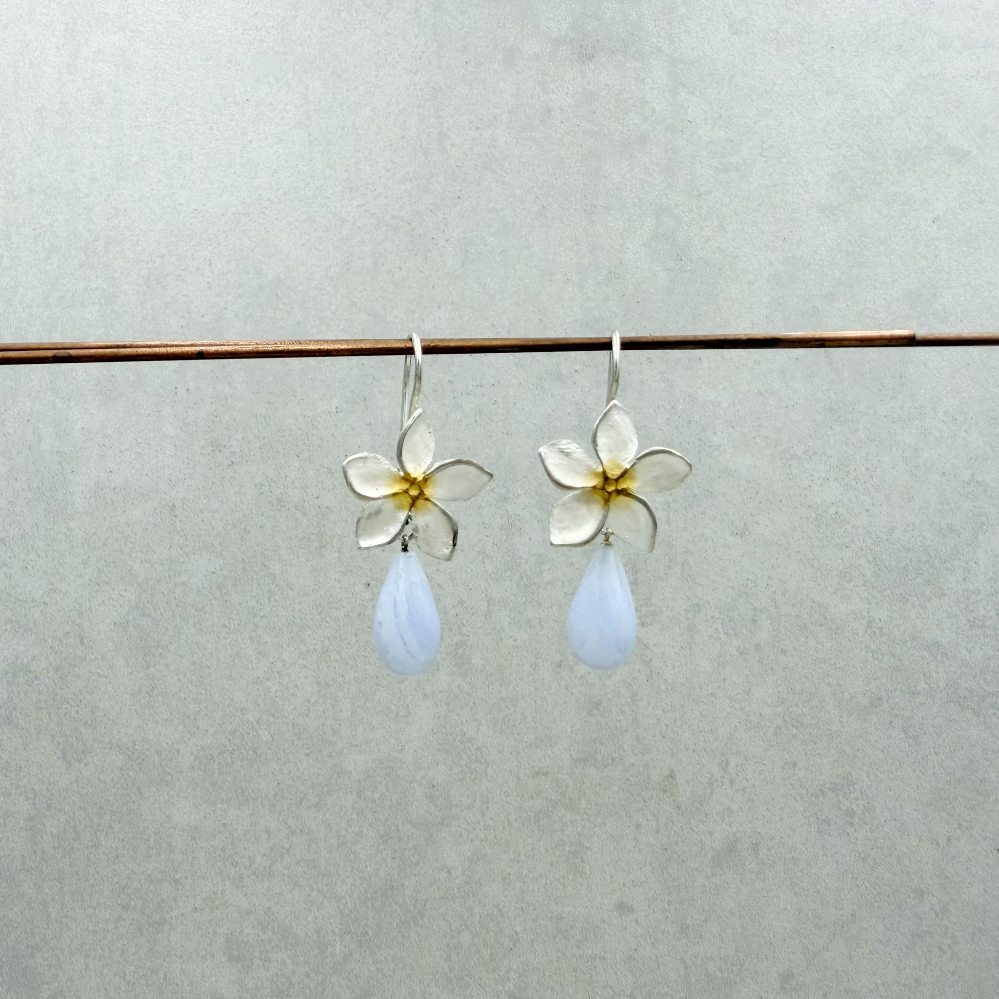 Frangipani-Blüten Ohrhänger mit hellblauen Chalcedonen. Die interessant gebänderten Edelsteine in Tropfenform sind facettiert und glitzern ganz leicht in der Bewegung. Frangipani-Blüten: ca. 1.5cm Chalcedon: ca. 15x8mm