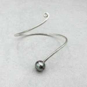 Geschwungener, handgeschmiedeter Armreif mit einer gebänderten Tahiti-Perle in schwarz-grau, 10-10.5mm. Durch die geschwungene Form sitzt der Armreif gut am Arm. Die Oberfläche ist mattiert. Bitte geben Sie im Checkout den Armumfang an.