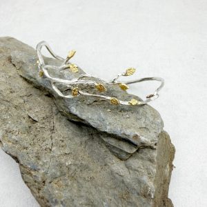 Kunstvoll gestalteter, geschwungener, handgeschmiedeter Armreif aus 925/- Silber mit feinen, vergoldeten Blättchen.