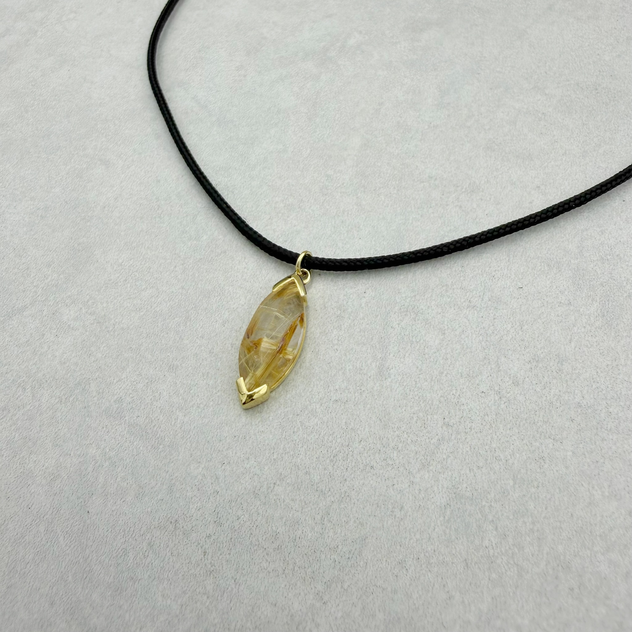 Handgefertigter Anhänger aus 585/- Gelbgold mit einem Fair Trade Rutilquarz im Navette Schliff. Fair funkelt mehr: der Edelstein kommt aus fairem und nachhaltigem Abbau. Der Anhänger ist kombiniert mit einem schwarzen Textil-Band mit einem goldenen Feddering-Verschluss (Gesamtlänge 42cm).
